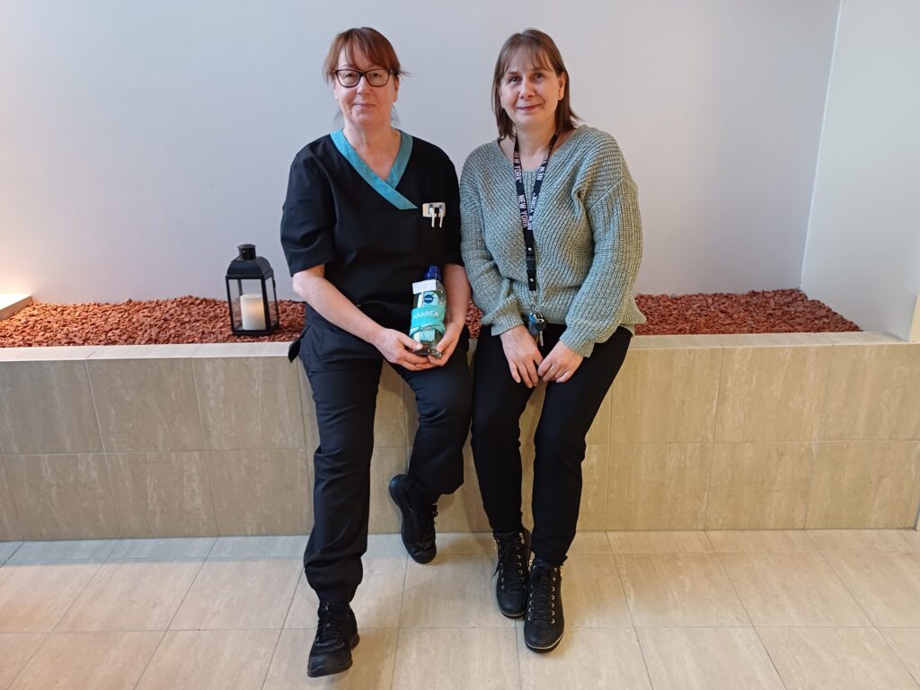 Anu Kinnunen ja palveluesihenkilö  Sari Mäkitalo istuvat vierekkäin. Heidän vieressään on kynttilälyhty ja Anulla on kädessä Sarin ojentamat lahjat